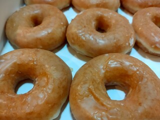 A close-up view of glazed donuts, showcasing their shiny surface and classic ring shape, arranged neatly in a box.