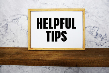 Blackboard with text "Helpful Tips" on a wooden shelf, set against a marble wall.
