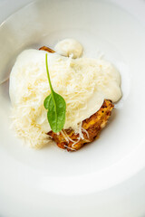 Grilled chicken breast topped with melted cheese and creamy white sauce, garnished with fresh spinach leaf. Served on a white plate. Close-up, isolated, appetizing presentation.