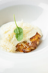 Grilled chicken breast topped with melted cheese and creamy white sauce, garnished with fresh spinach leaf. Served on a white plate. Close-up, isolated, appetizing presentation.