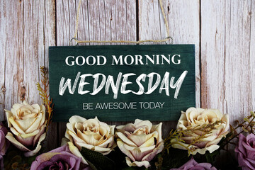 Good Morning Wednesday Be Awesome Today text written on wooden plank with flower decoration on...