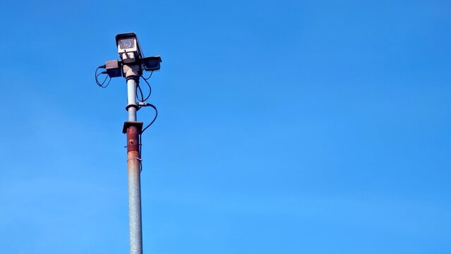 A single security camera on a rusty metal pole against a clear blue sky, a powerful symbol of surveillance, safety, and modern technology