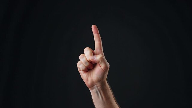 Hand raised with a pointing finger against a dark background  