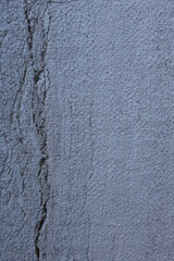 Textured surface of a gray wall showing cracks and variations in color over time during daylight