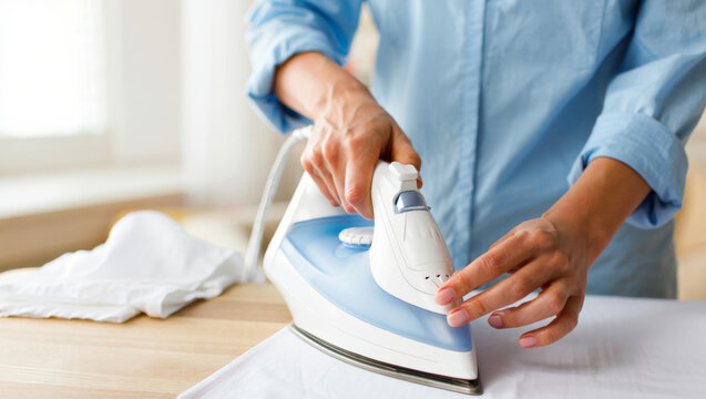Person ironing white shirt with modern steam iron on wooden surface, concept of household chores, domestic work, cleanliness, garment care and wrinkle free clothing
