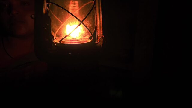 A calm, thoughtful Indian woman holds a glowing kerosene lantern in the warm darkness, her pensive expression evoking mystery, hope, and quiet strength as the soft light illuminates the night.