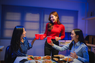 Diverse group of women colleagues celebrating a party after work, toasting with cups in an office environment