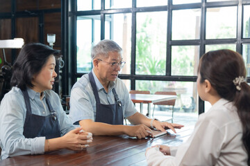 Small business restaurant owner senior couple with staff teamwork meeting, husband and wife guiding young workers, Asian management discussion service training in dining area professional lifestyle