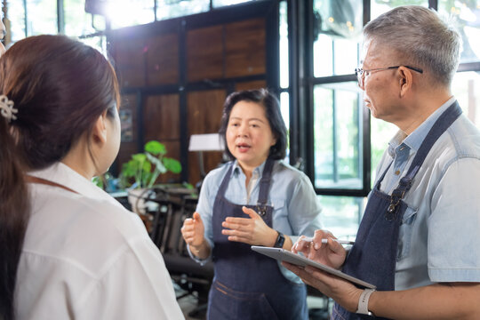 Restaurant small business senior owner husband, wife training staff teamwork, apron uniform service preparation management consultation, Asian couple coaching employees hospitality development