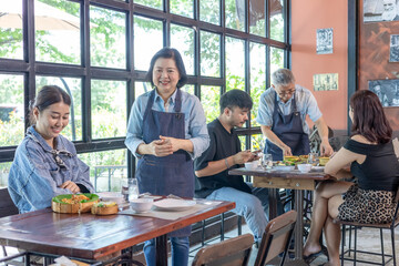 Restaurant small business senior couple owners taking food order from customers using digital tablet technology, teamwork service table, Asian husband and wife management professional support