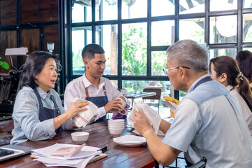 Small business restaurant owner senior couple guiding staff in apron, teamwork service inside dining area, Asian husband and wife management training with communication and customer care, startup