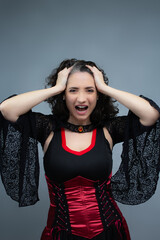 Mad witch with hands on her head, worried about her Halloween tricks. Suitable for spooky season, witchcraft and fairy tale villain. Vertical studio portrait with copy space.