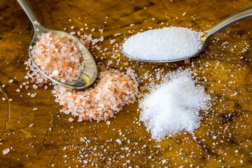Two teaspoons of respectively pink Himalayan salt and white table salt, surrounded by spilled salt