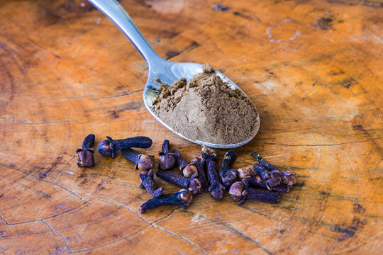 A teaspoon with ground cloves, with a few whole cloves spilled in the foreground. - Powered by Adobe