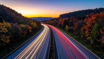 Highway at dusk with red and white light trails through forest and colorful sky.