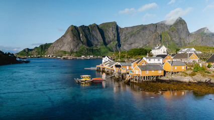 Vibrant orange cabins dot the shoreline of Sakrisoy in Lofoten, Norway, surrounded by towering...