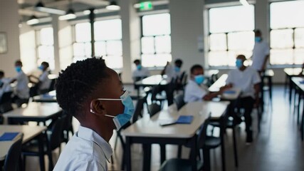 Boy in classroom with other students. Students sitting in a classroom with masks. Boys learning about the pandemic in a school. A student in a classroom alongside his peers lifestyle. - Powered by Adobe