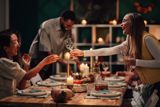 Friends celebrating thanksgiving, passing wine glasses at decorated table - Powered by Adobe