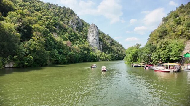 Danube river flowing through the Iron Gates gorge in Romania, featuring the ancient Dacian King Decebalus sculpture carved into the mountain, with small boats cruising on the water