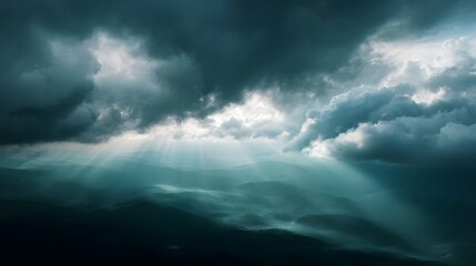 Dramatic sunbeams pierce through dark storm clouds over a misty mountain landscape