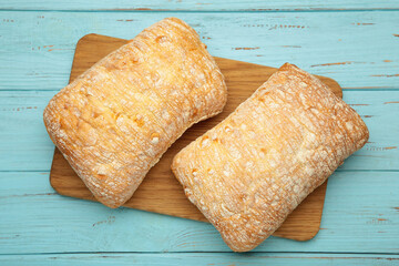 Ciabatta rustic bread on cutting board on blue background.