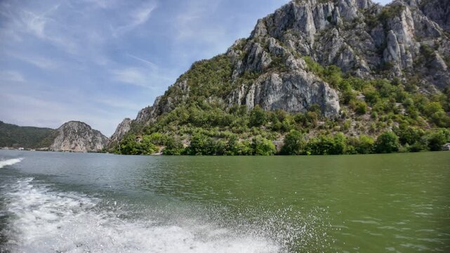 Danube river flowing through the Iron Gates gorge, with steep rocky mountains covered in green vegetation rising from the water, creating a dramatic natural landscape between Serbia and Romania