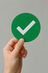 A hand holds a green circular sign with a white checkmark symbol on it.