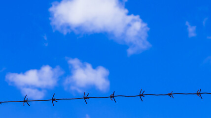 Barbed wire stretches across a vibrant blue sky with fluffy white clouds on a bright sunny day