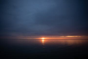 Scenic sunset over calm water with dramatic clouds, golden sunlight reflecting on the surface, creating a peaceful and atmospheric seascape.