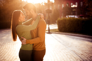 Happy couple embraces warmly during a serene autumn afternoon in a park setting with sunlight...