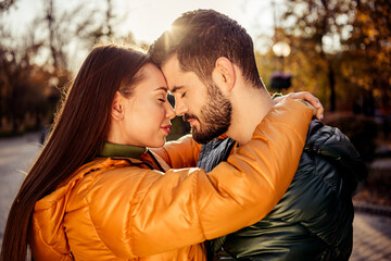 Young couple embracing lovingly outdoors during autumn in a sunny park setting, surrounded by seasonal foliage and warm tones