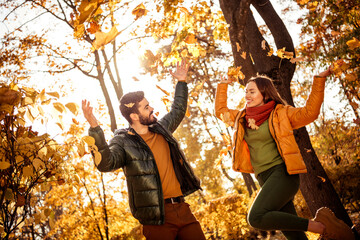 Couple joyfully enjoying autumn in a sunny park surrounded by vibrant fall foliage, expressing happiness and love