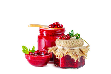 Jar and bowl of lingonberry jam with berries, leaves and wooden spoon isolated on white background.