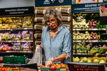 Senior woman choosing fresh tomatoes in grocery store