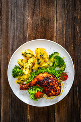 Oven roasted chicken leg with boiled potatoes and boiled broccoli on wooden table	