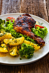 Oven roasted chicken leg with boiled potatoes and boiled broccoli on wooden table	