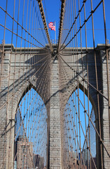 Obraz premium Iconic view of New York city with Waving American Flag on the top of Tower of Brooklyn Bridge and steel cables