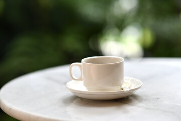 White ceramic cup on saucer with spoon on marble table in garden morning light, peaceful beverage moment for relaxing or breakfast