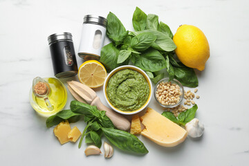 Fresh pesto sauce in bowl, ingredients and squeezer on white marble table, flat lay