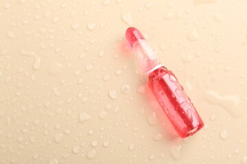 Glass ampoule with cosmetic product and water drops on beige background, top view. Space for text