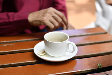 Empty white coffee cup on saucer with teaspoon on wooden table, hand blurred in background conveying calm morning moment
