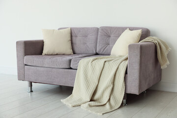 Comfortable gray sofa with blanket and cushions in room