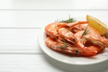 Delicious seafood dish. Tasty grilled shrimps served with rosemary and lemon on white wooden table, closeup. Space for text