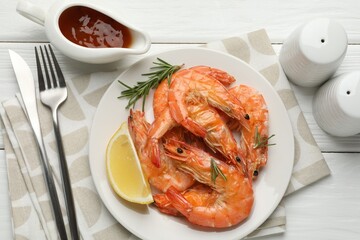 Tasty grilled shrimps served with rosemary, sauce and lemon on white wooden table, flat lay. Delicious seafood dish