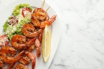 Skewers with tasty grilled shrimps, salad and lemon slice on white marble table, top view with space for text. Delicious seafood dish