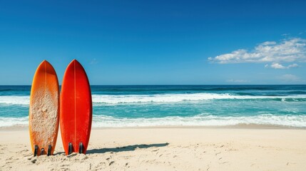 Two red surfboards on a sandy beach with a clear blue sky and turquoise ocean in the background.