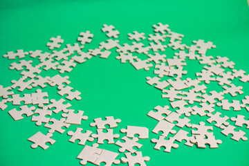 Scattered white jigsaw puzzle pieces on green background, representing incomplete projects and the challenge of finding the solution