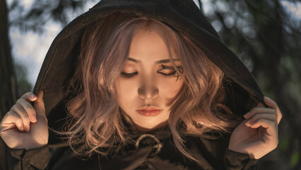 Mysterious woman with rose gold hair wearing a dark hooded cloak in an enchanted forest, perfect for fantasy storytelling and atmospheric projects © STMJ STUDIO