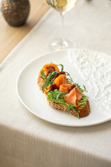 Gourmet bruschetta with salmon, avocado spread and arugula on a sesame baguette slice, served on white plate