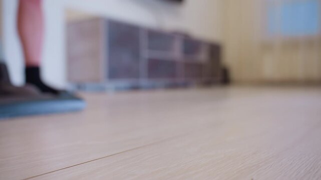 Close up of vacuum cleaner head gliding over light wooden floor with person in black socks standing in blurred background, concept of household chores, cleaning routine and modern home hygiene